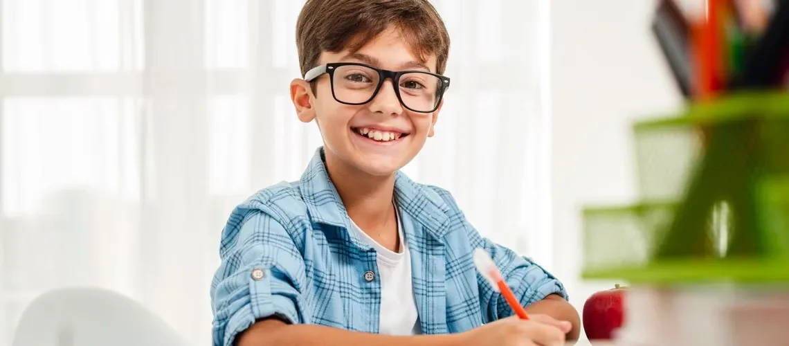 Menino de óculos sorrindo em uma mesa de estudos