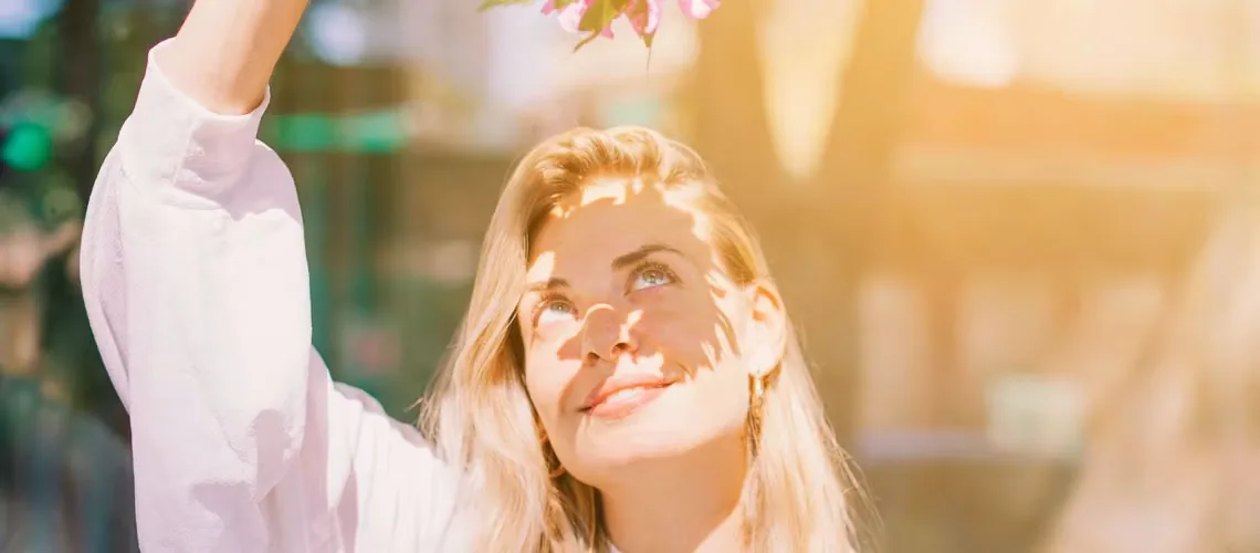 Mulher sorrindo de braços abertos sob o sol